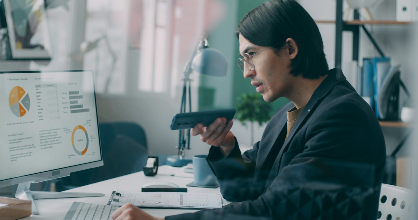 Man in blazer and glasses analyzes computer data while on phone.