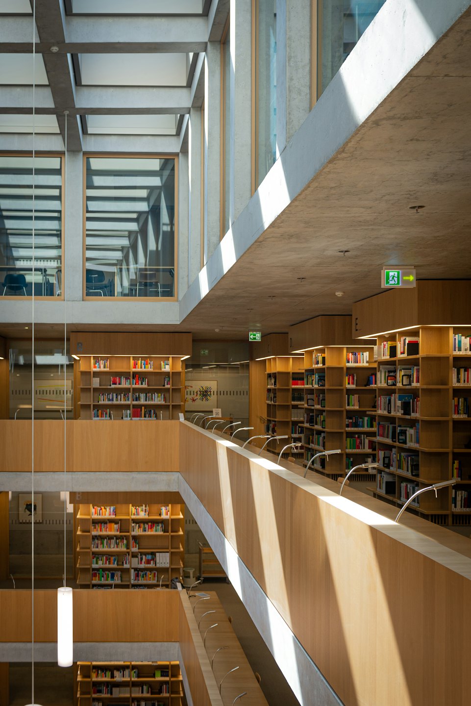 Modern library interior with wooden bookshelves and large windows.